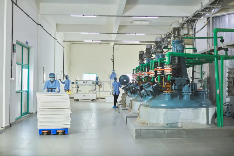 Production hall with reactor vessels, green pipework and stacked material on a pallet