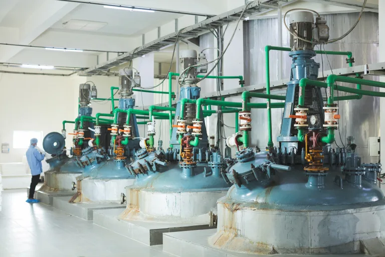 Row of reactor vessels with green pipework, with operators at work